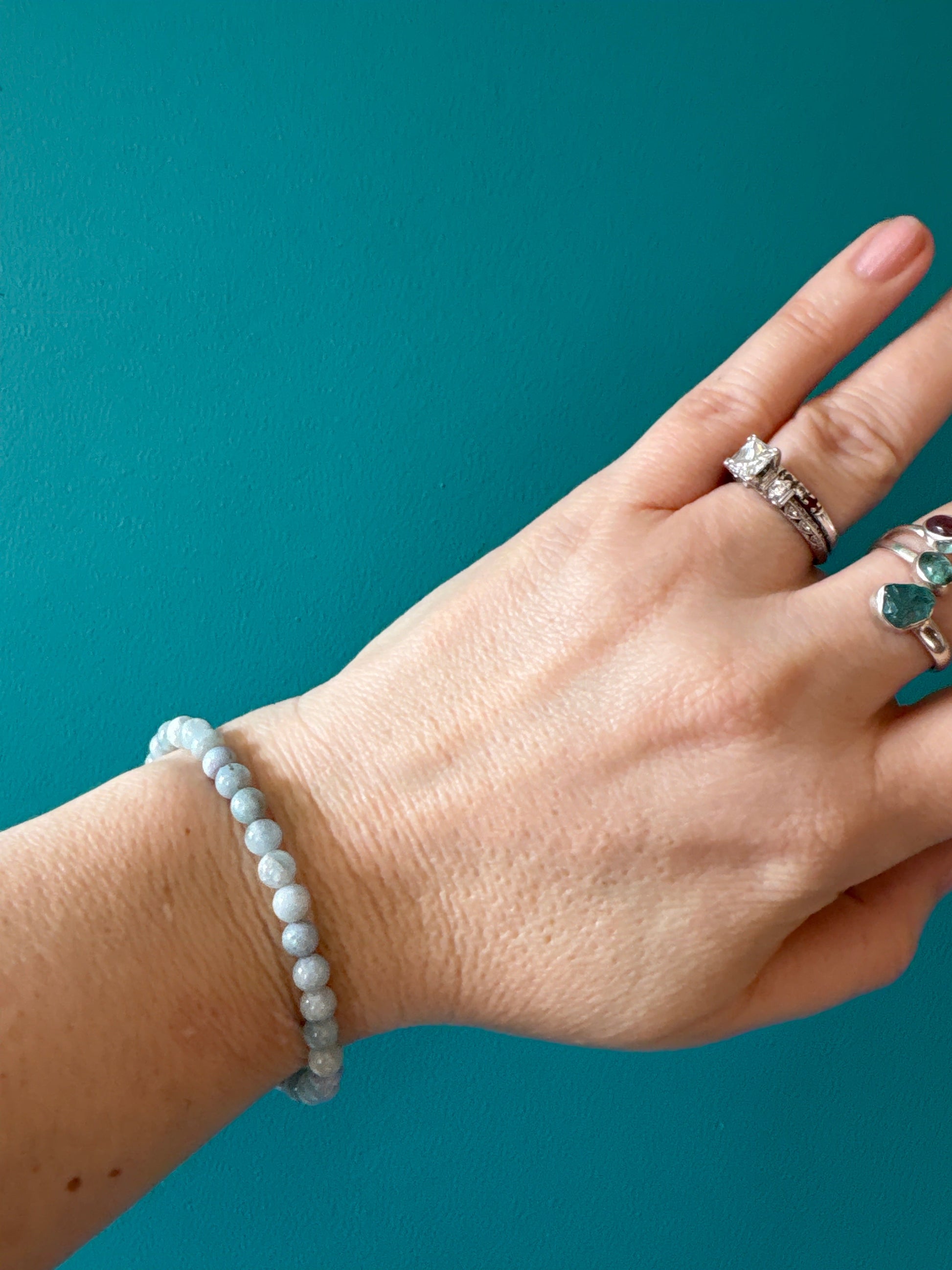 Aquamarine bead bracelet on wrist with silver rings against teal background