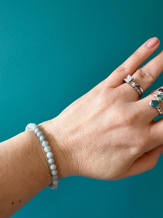 Aquamarine bead bracelet on wrist with silver rings against teal background