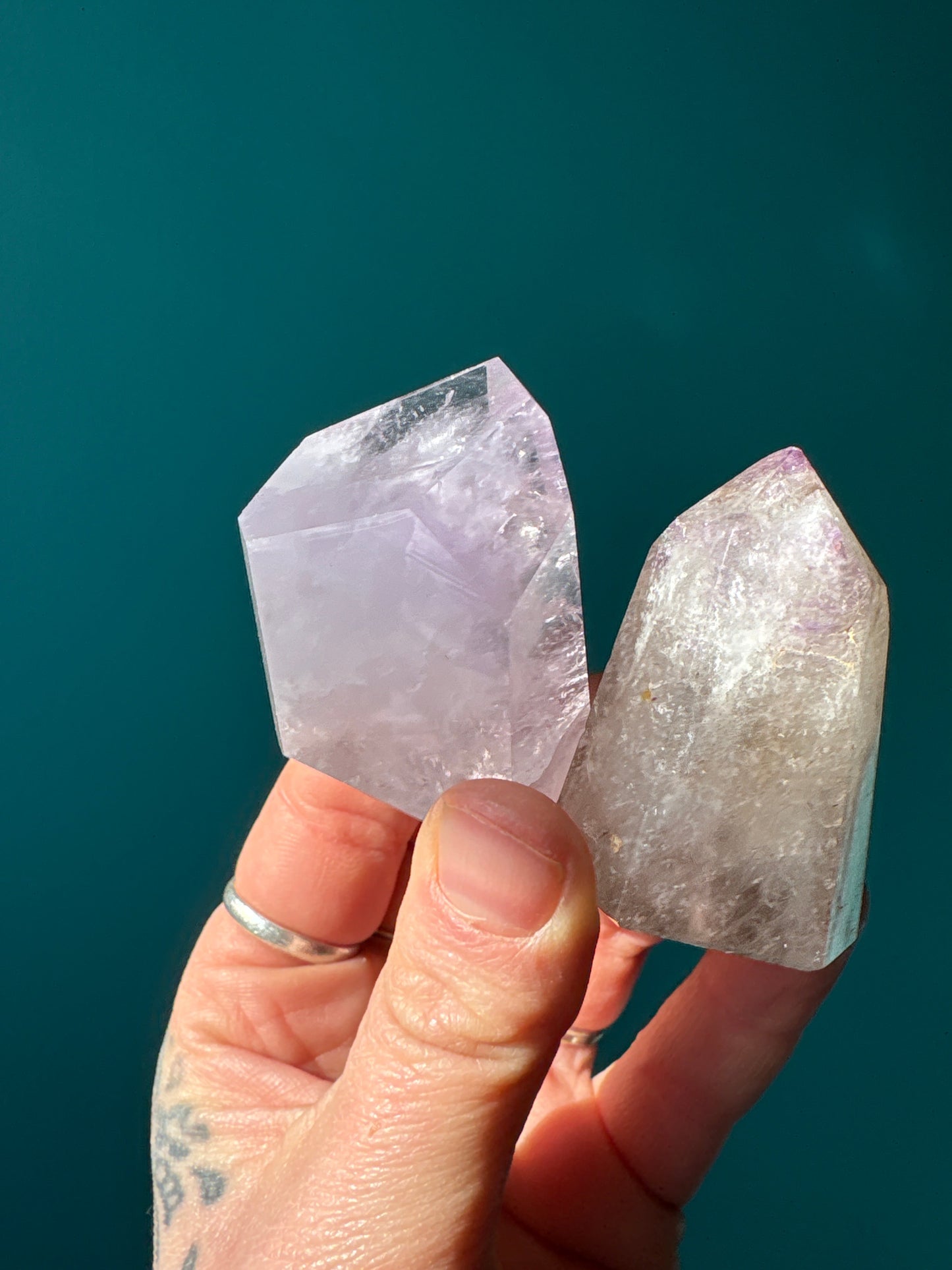 Hand holding two natural amethyst towers with pointed shapes against a teal background