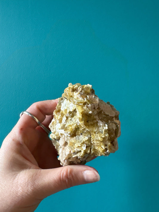 Hand holding raw star mica mineral with sparkly texture against teal background