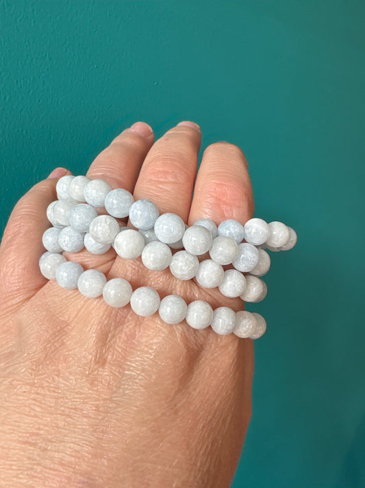 Close-up of hand holding multiple strands of 8mm light blue celestite bead bracelets for mental clarity and stress relief
