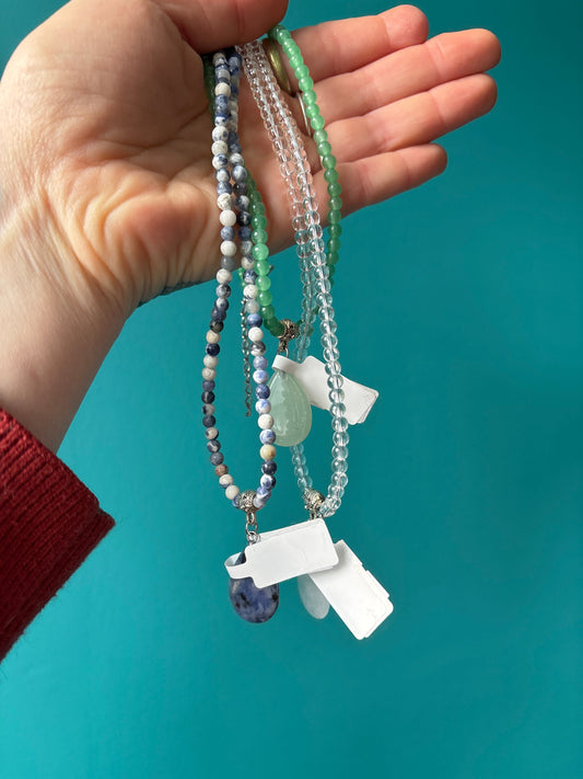 Teardrop choker necklace with shimmering pendants on delicate chain held against teal background