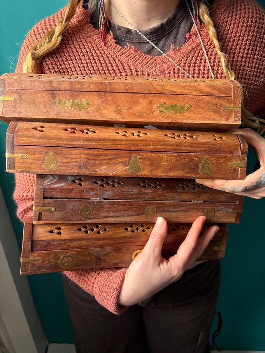 Person holding stacked wooden coffin incense burners with spiritual designs