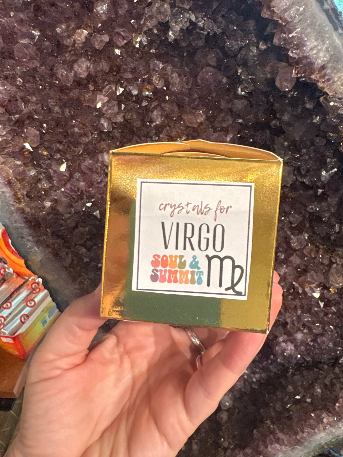 Virgo Crystal gift box held in hand with amethyst crystal background and Virgo zodiac symbol on the packaging