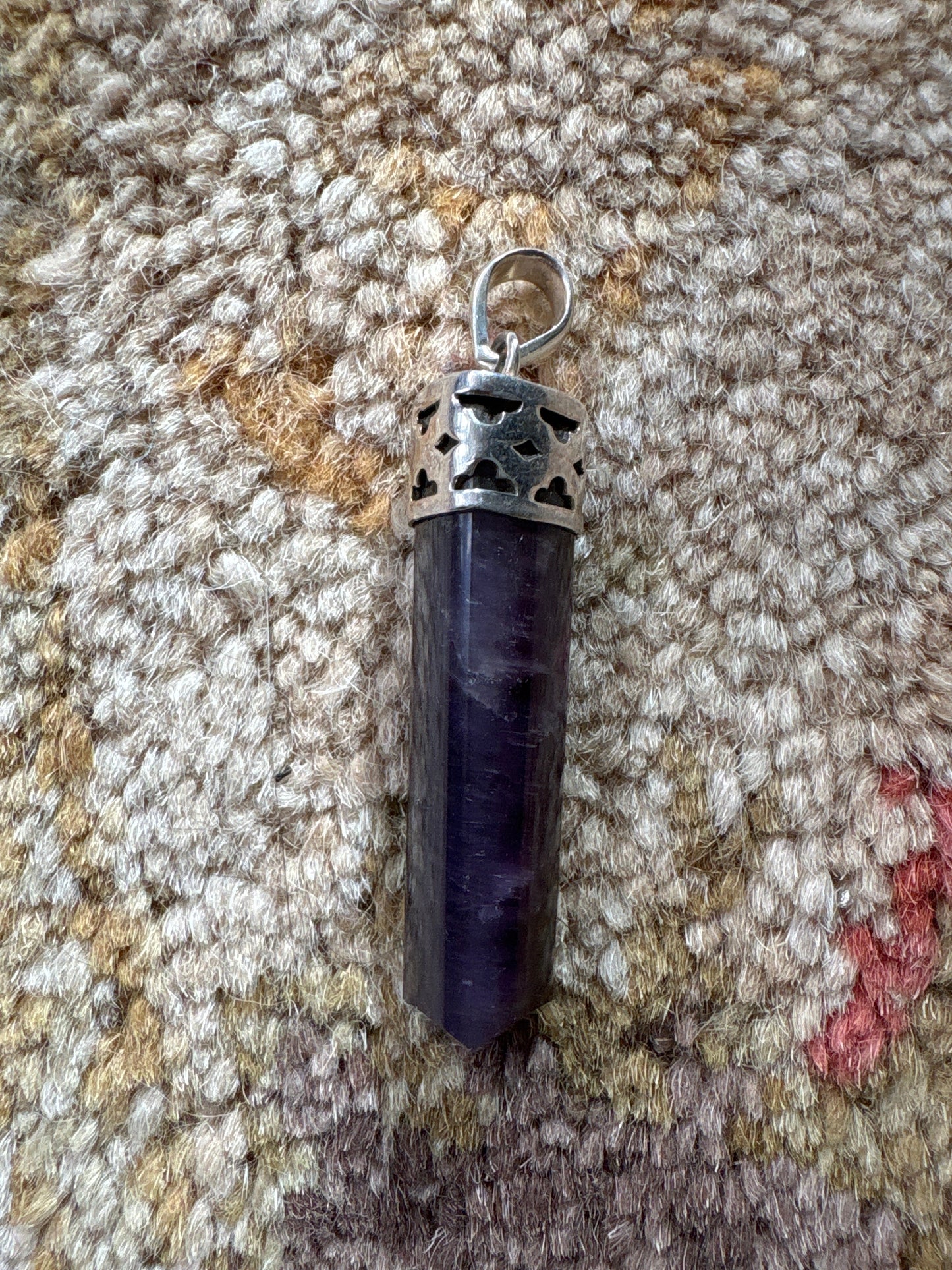 Amethyst polished point pendant with silver cap on textured fabric background