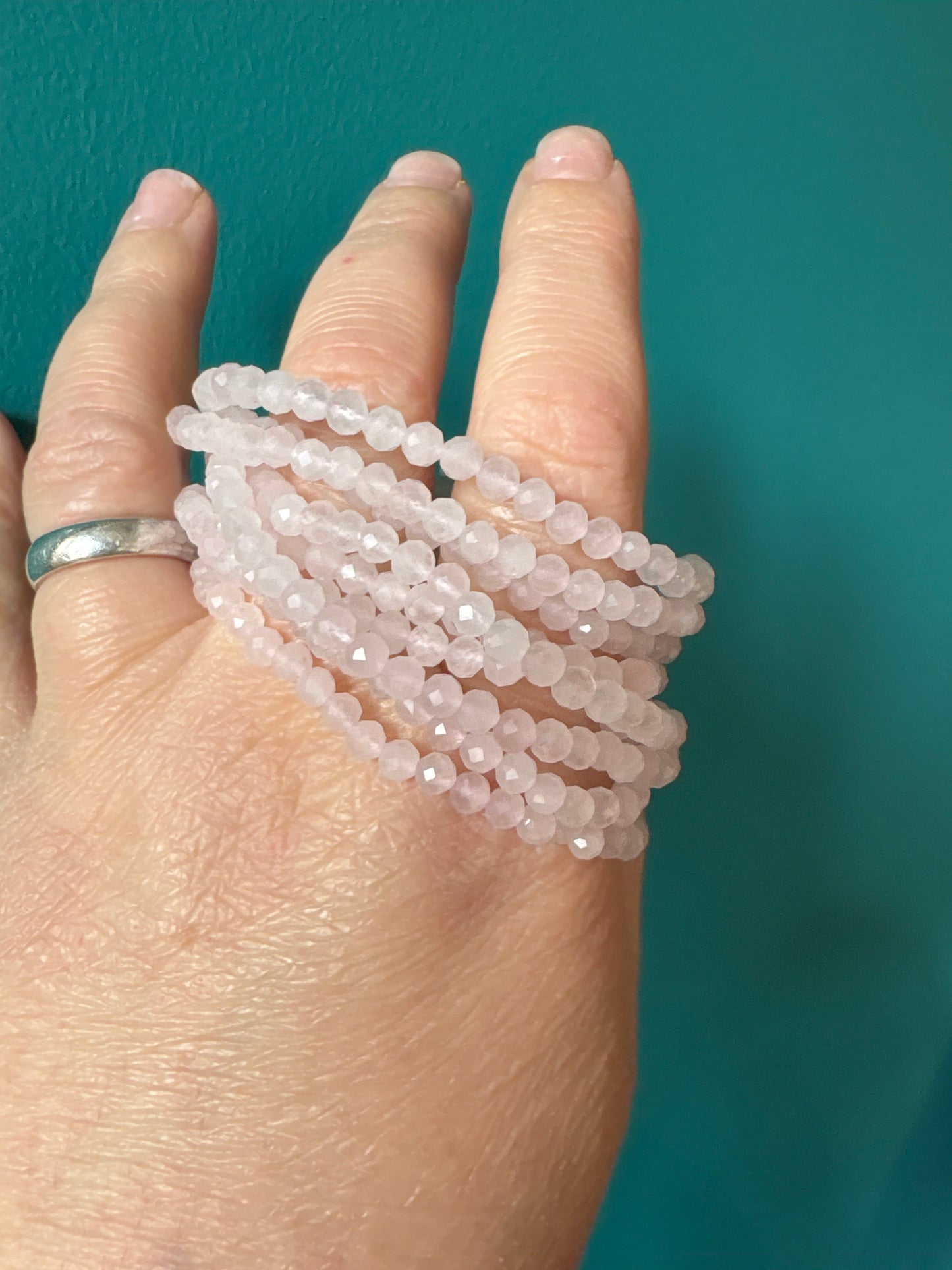 Close-up of faceted 4mm rose quartz bracelet beads worn on hand against teal background