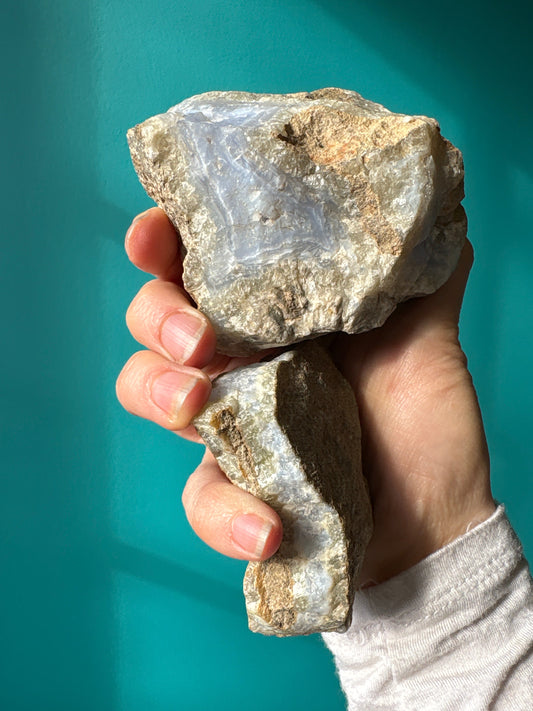 Hand holding raw blue lace agate stones with natural light and teal background