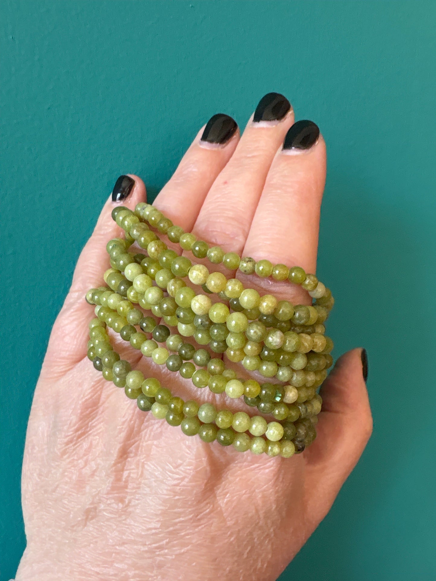 Bracelet Jade 4mm green beaded bracelet worn on hand with dark nail polish on teal background