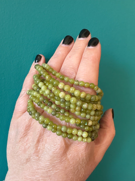 Bracelet Jade 4mm green beaded bracelet worn on hand with dark nail polish on teal background