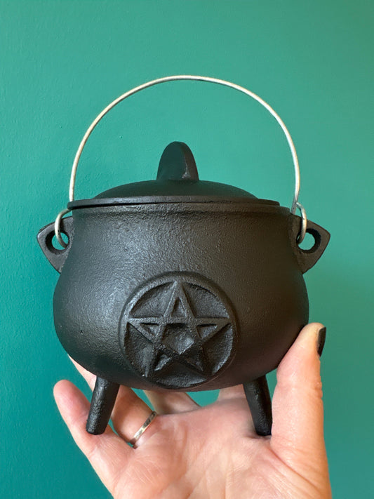5.5 inch cast iron cauldron with pentacle design held in hand against teal background