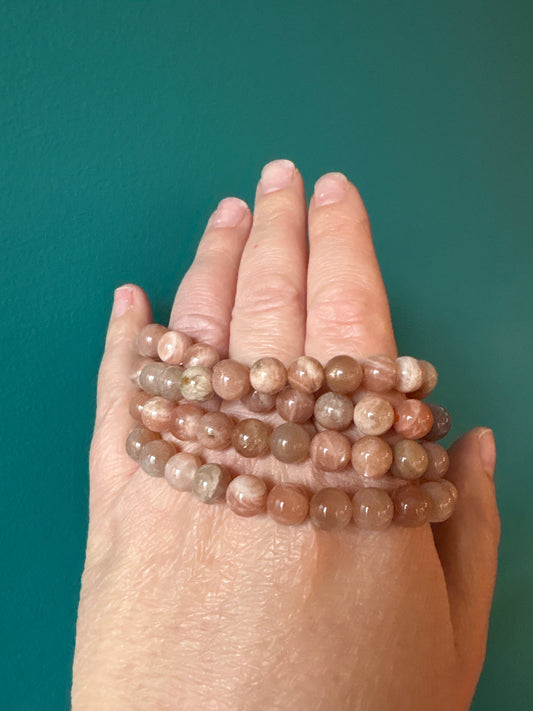 Sunstone Bracelet with polished 8mm beads enhancing intuition and creativity on hand against teal background