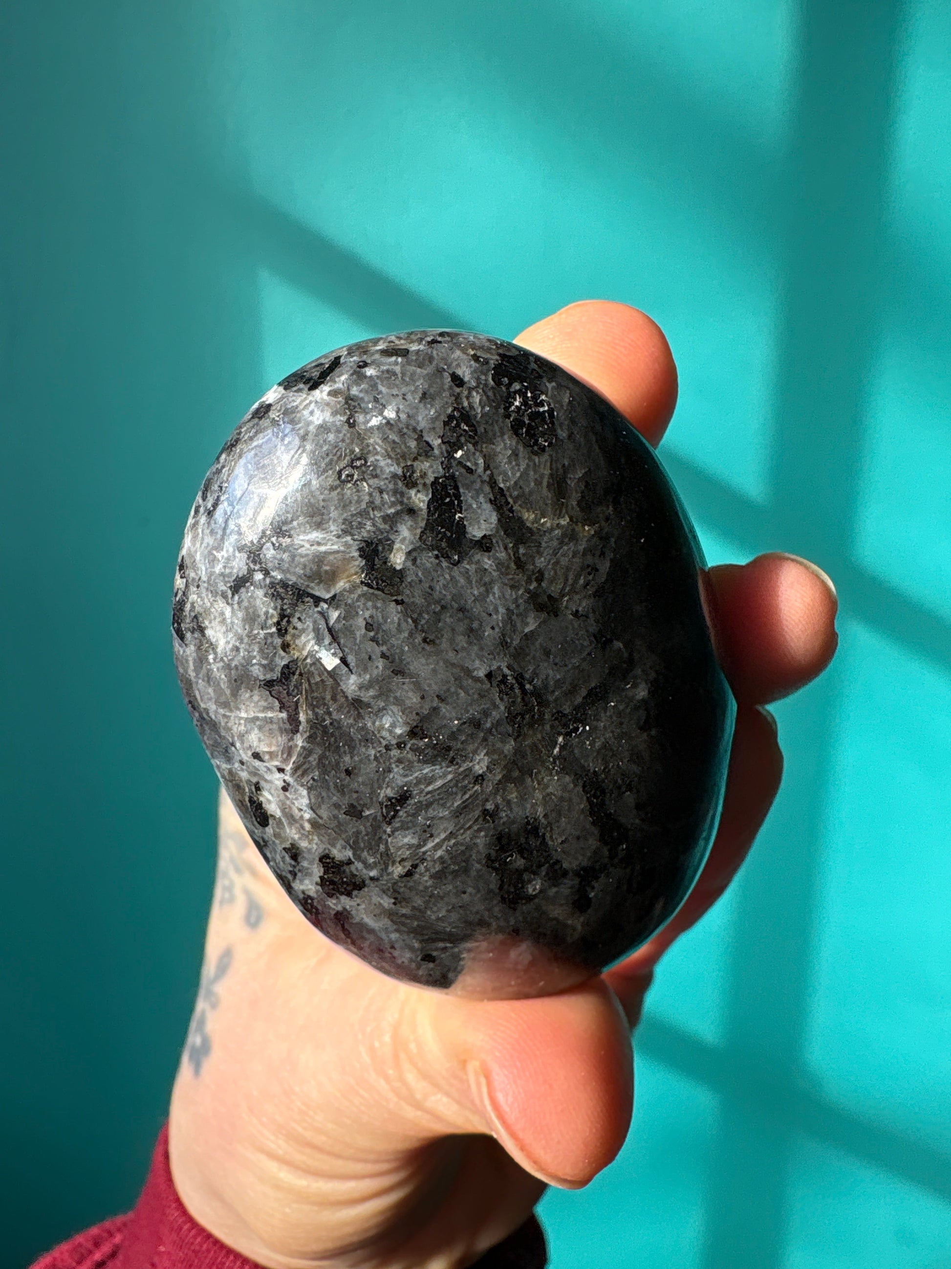 Hand holding polished Larvakite palm stone with a blue-green background for meditation and healing