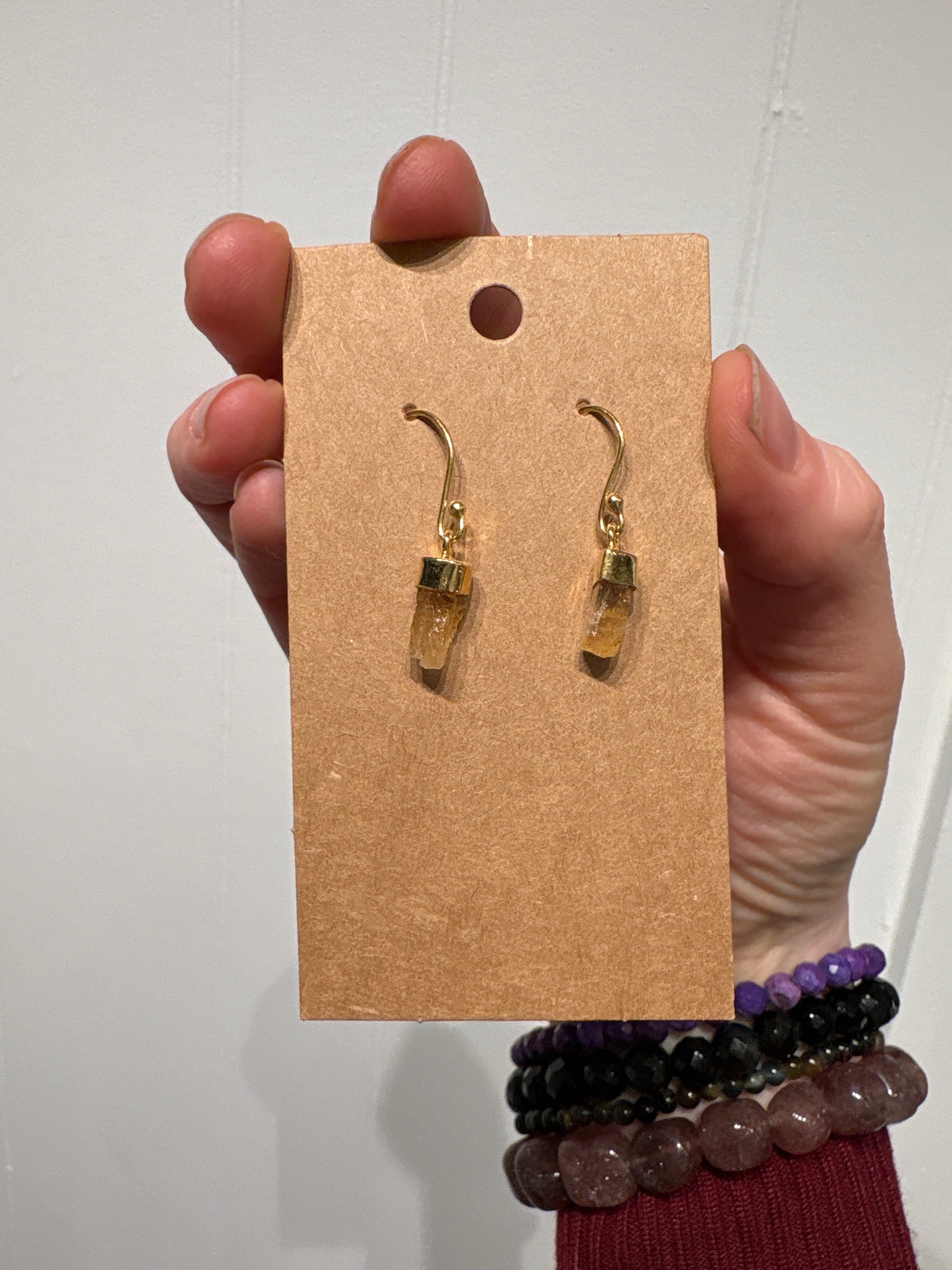 Hand holding card displaying gold topaz earrings with hook design