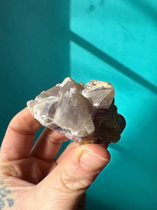Hand holding a cluster of lavender amethyst crystals against a teal background