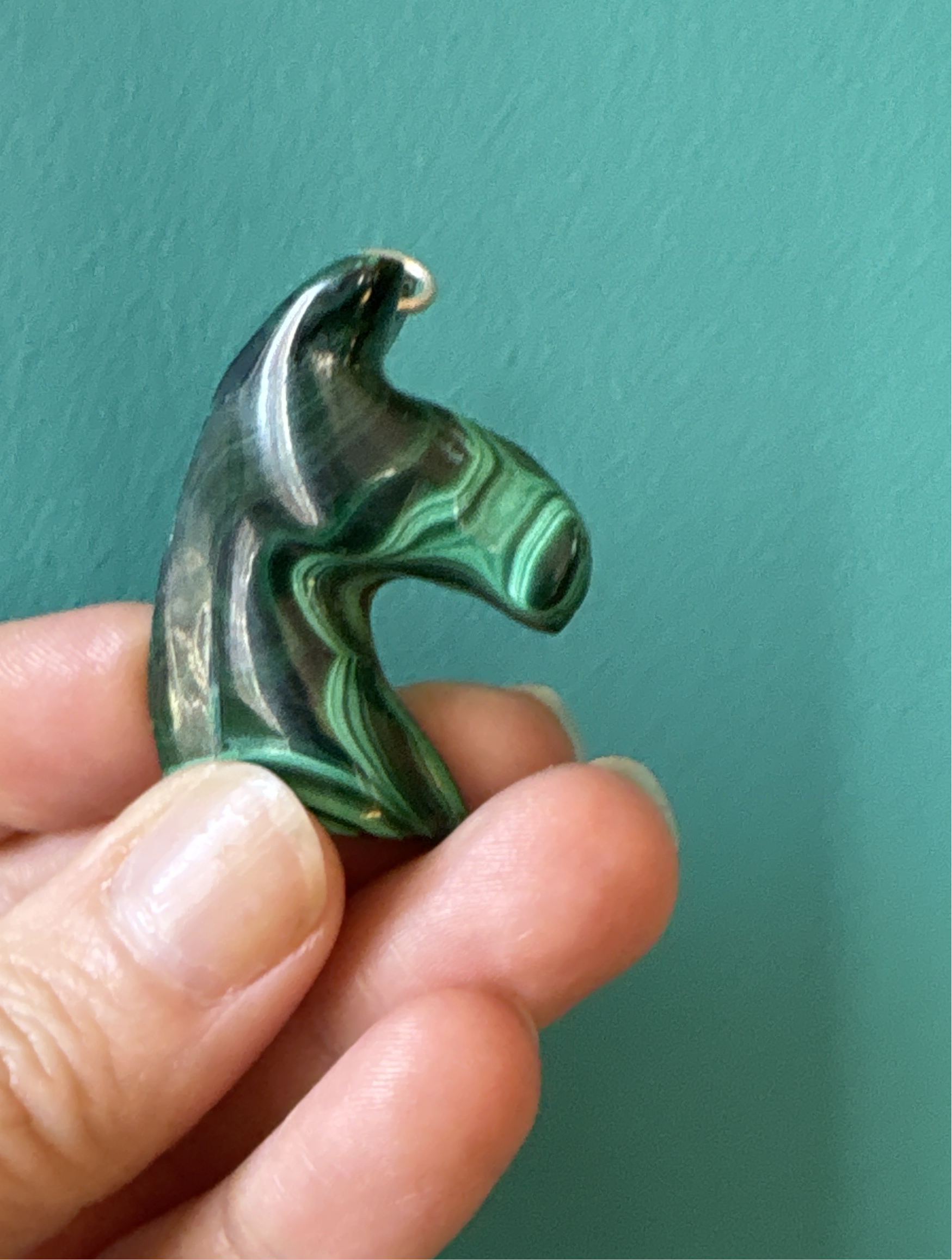 Hand holding a green Malachite horse pendant with natural stone patterns against a teal background
