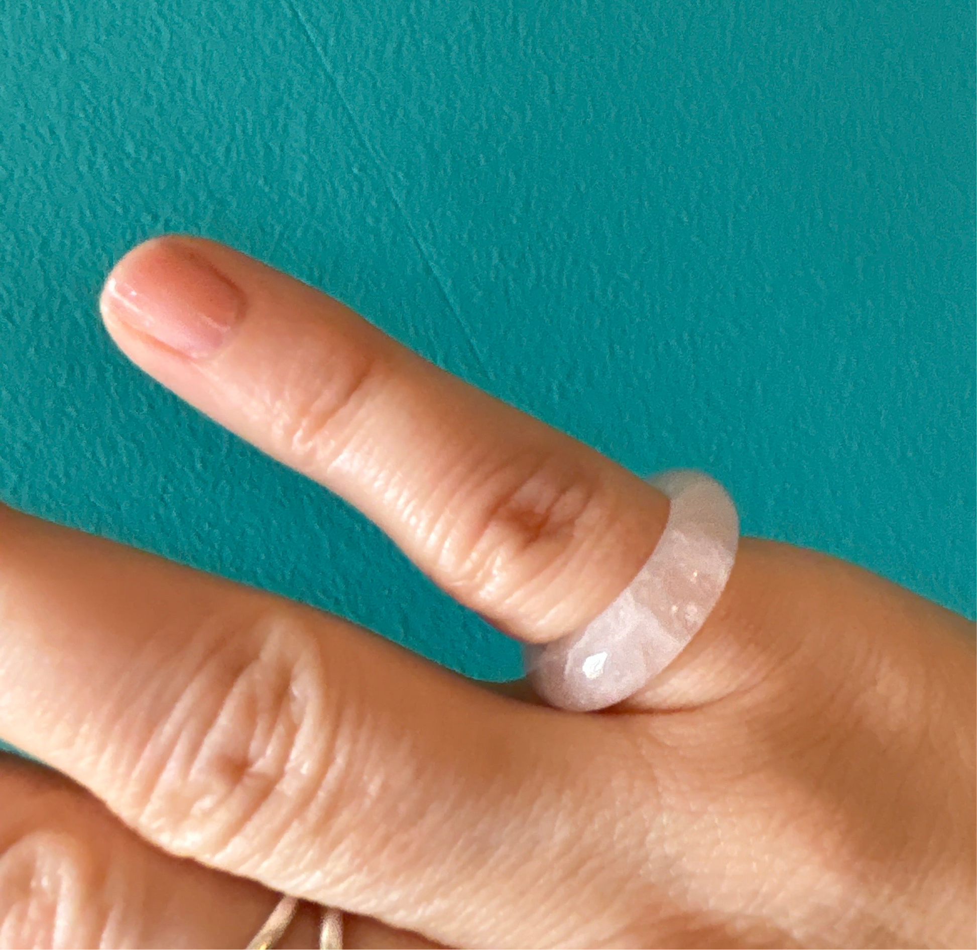 Close-up of a finger wearing a polished rose quartz ring rose with a smooth texture against a teal background