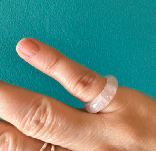 Close-up of a finger wearing a polished rose quartz ring rose with a smooth texture against a teal background