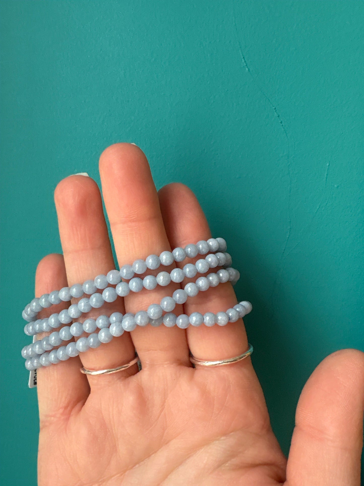 Hand holding a multi-strand Angelite Bracelet made of smooth light blue beads against a teal background