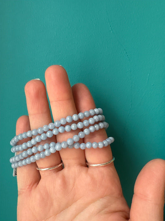 Hand holding a multi-strand Angelite Bracelet made of smooth light blue beads against a teal background