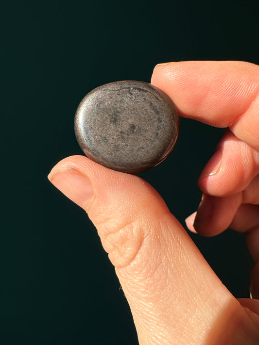 hand holding a smooth tumble hematite med stone against dark background