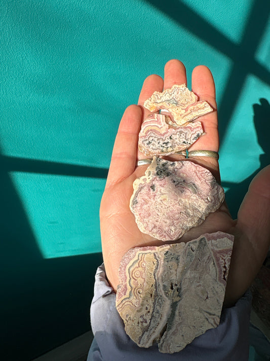 Rhodochrosite slab with pink and red hues showcasing unique natural patterns in hand against turquoise background