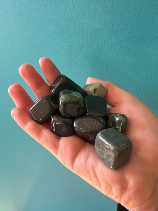 Hand holding smooth tumble jade stones against a blue background