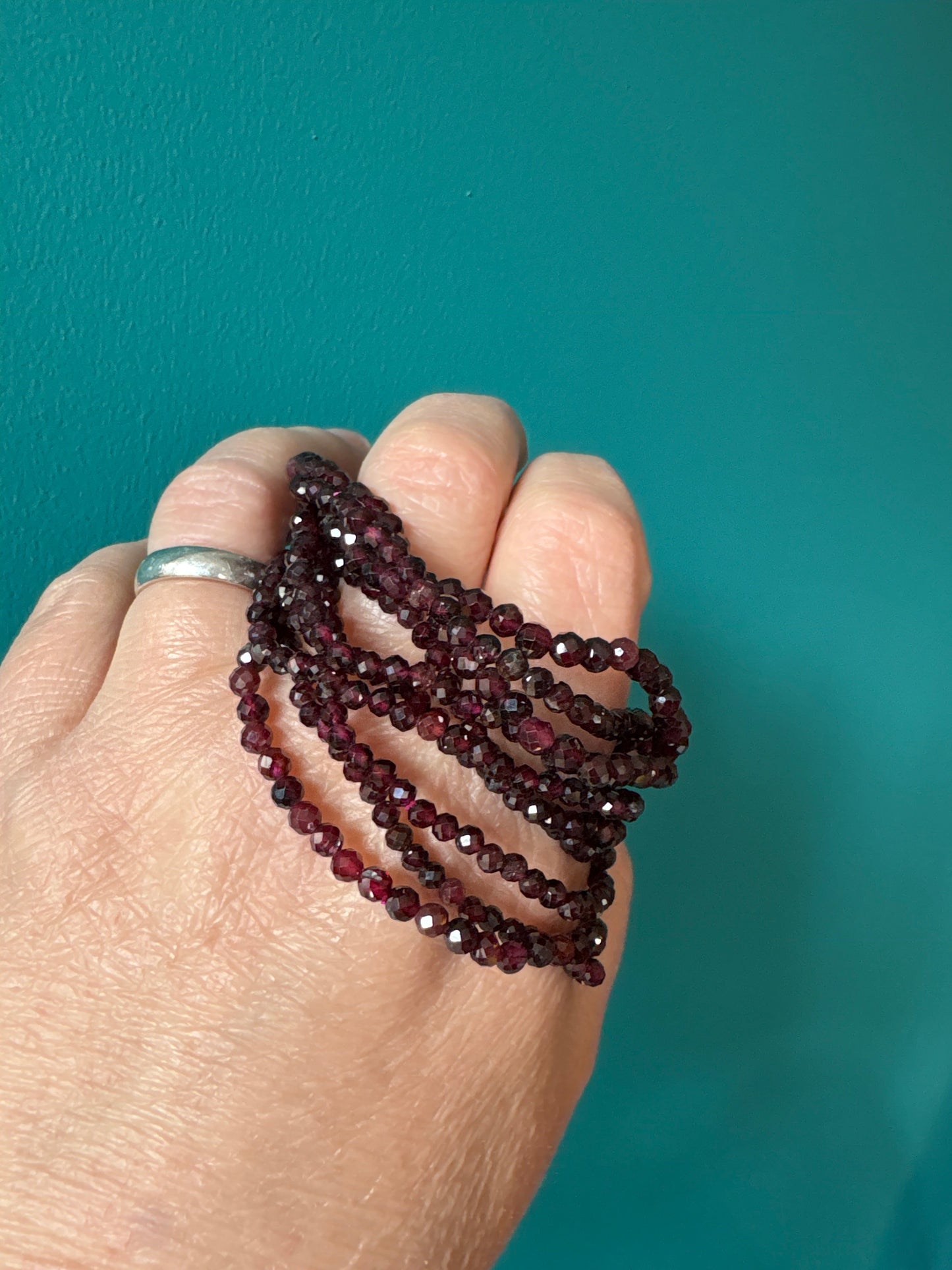 Faceted 4mm garnet gemstone bracelet wrapped around hand with teal background