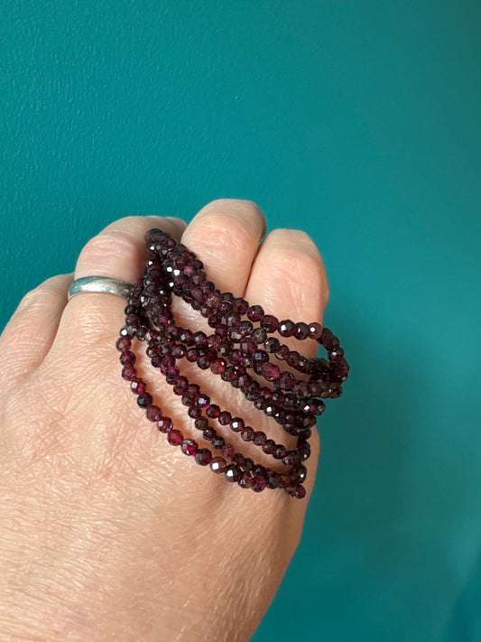 Faceted 4mm garnet gemstone bracelet wrapped around hand with teal background