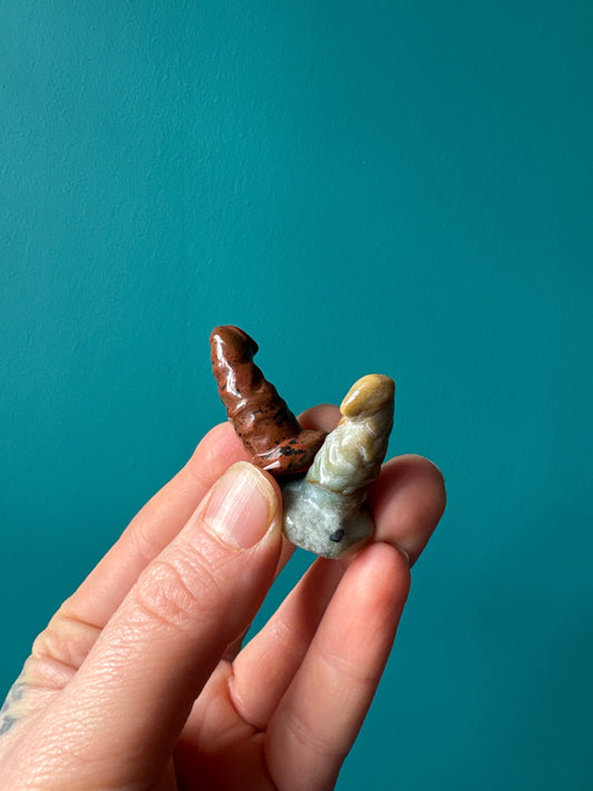Hand holding two small wizard hat crystals in brown and beige colors against teal background