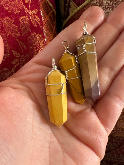Close-up of three Mookaite pendant stones wrapped in wire held in a hand