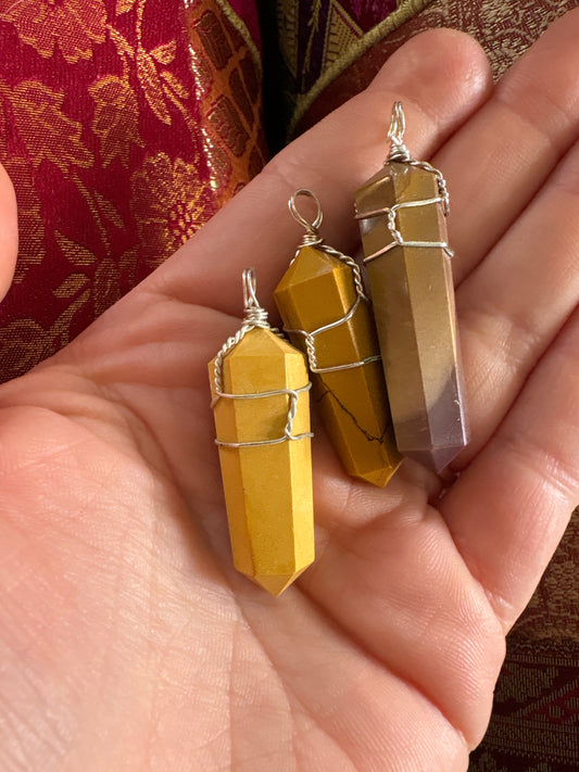 Close-up of three Mookaite pendant stones wrapped in wire held in a hand