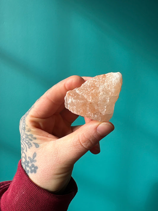 Hand holding a rough Himalayan Salt Chunk against a teal background