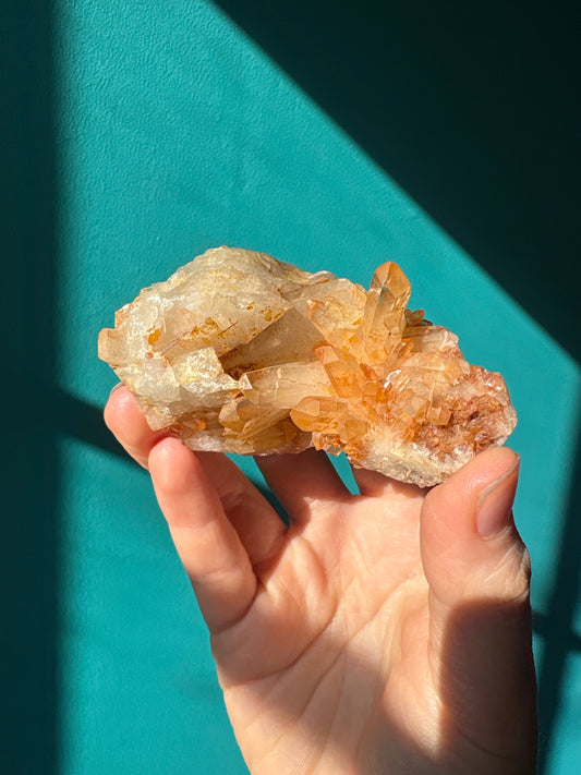 Hand holding a vibrant tangerine quartz cluster against a teal background