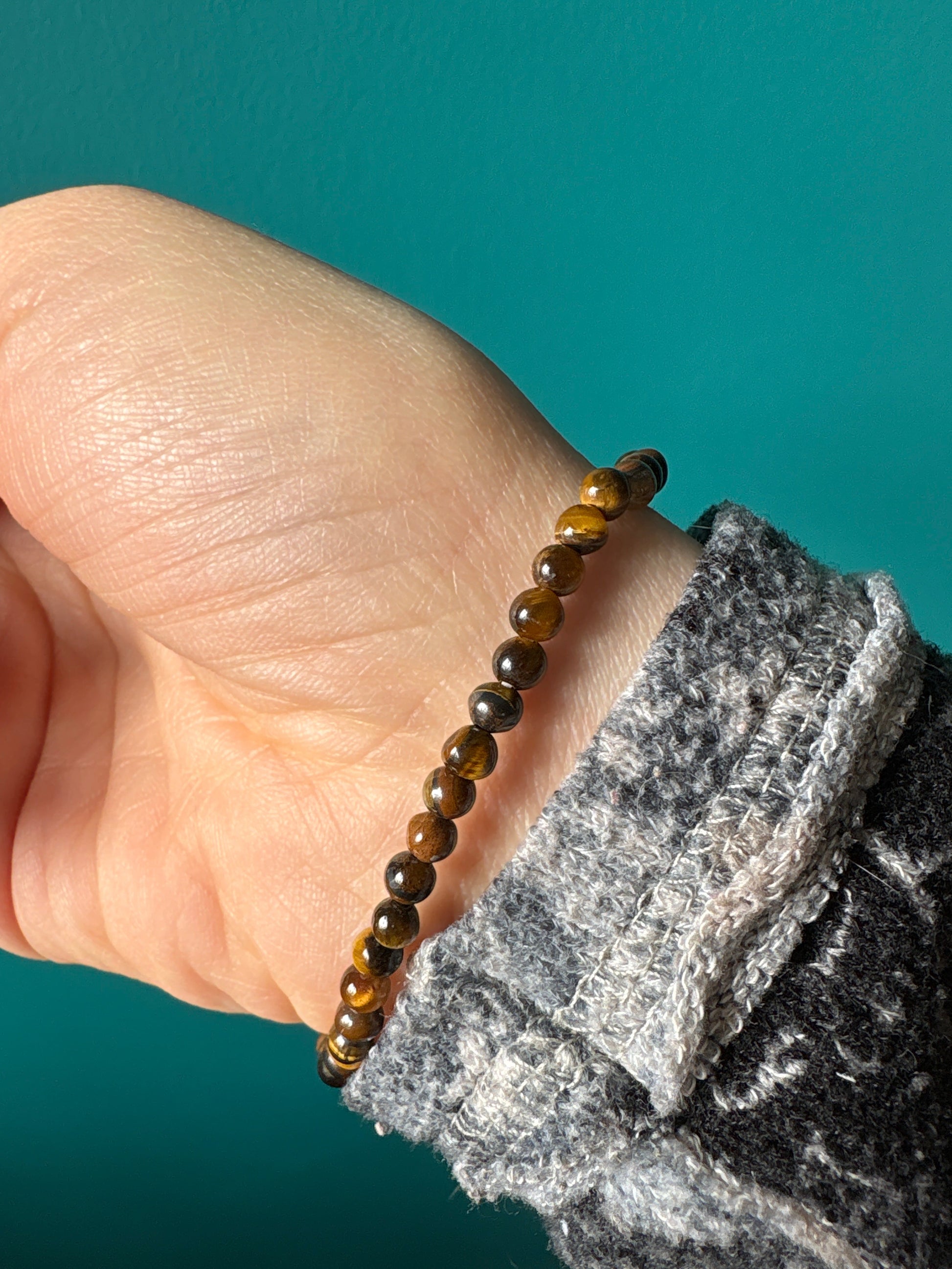 Tigers eye bracelet with polished round beads on wrist against teal background