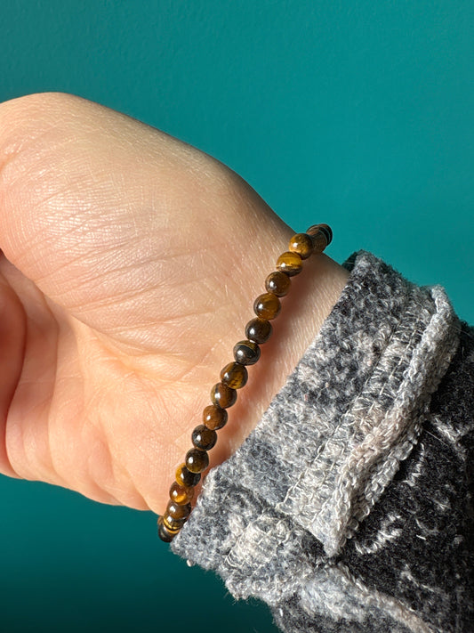 Tigers eye bracelet with polished round beads on wrist against teal background
