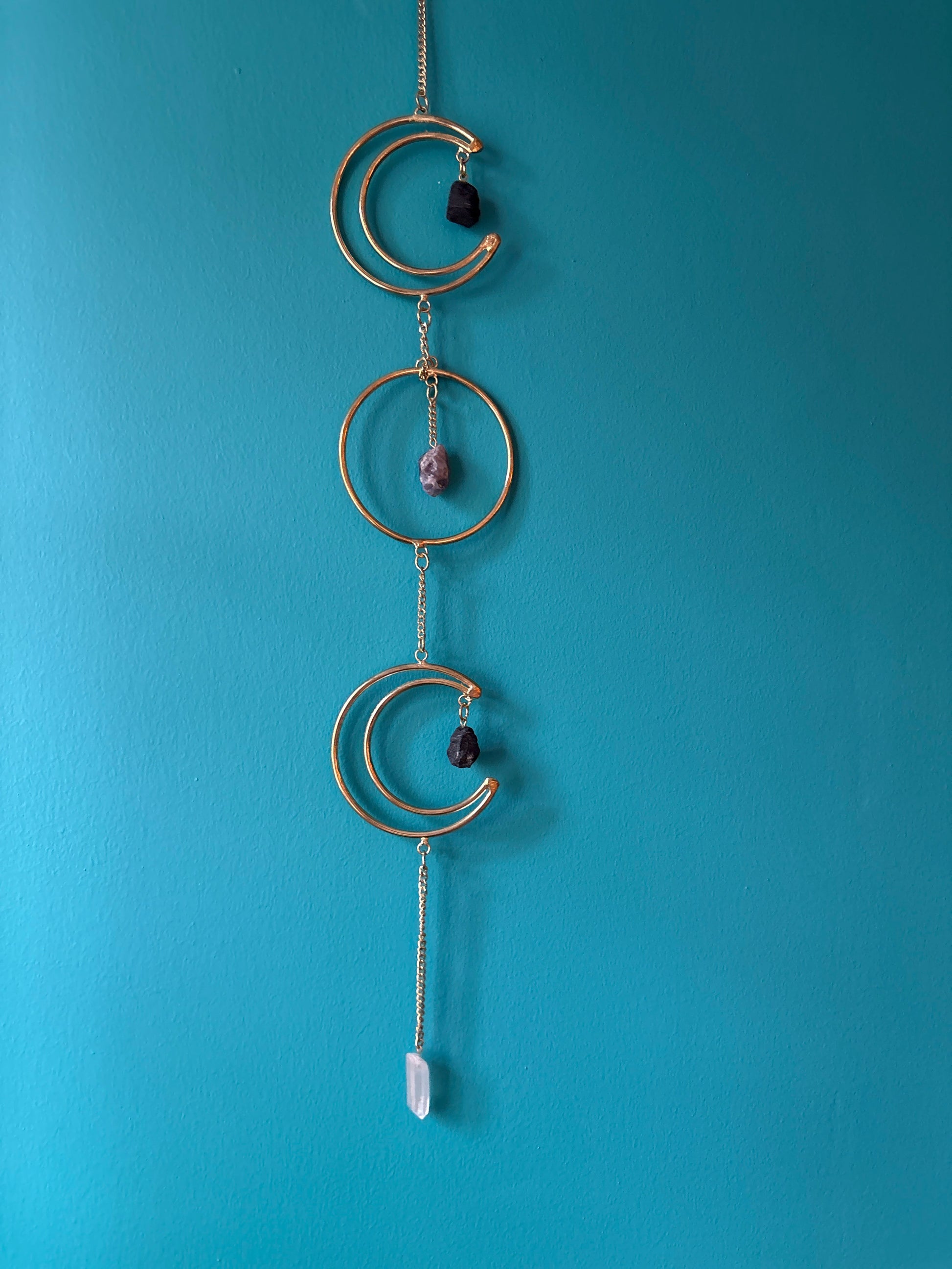 Gold wire hanging triple moon wall decor with stones against blue wall