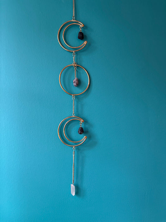 Gold wire hanging triple moon wall decor with stones against blue wall