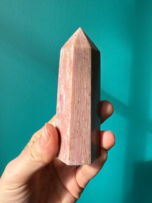 Hand holding a polished pink amethyst tower crystal against a turquoise background