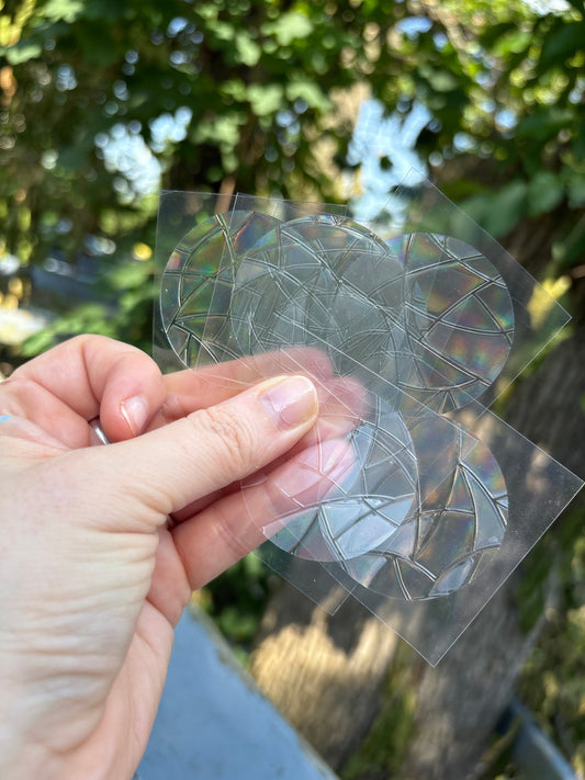 Hand holding transparent Rainbow Window Clings with holographic rainbow patterns outdoors