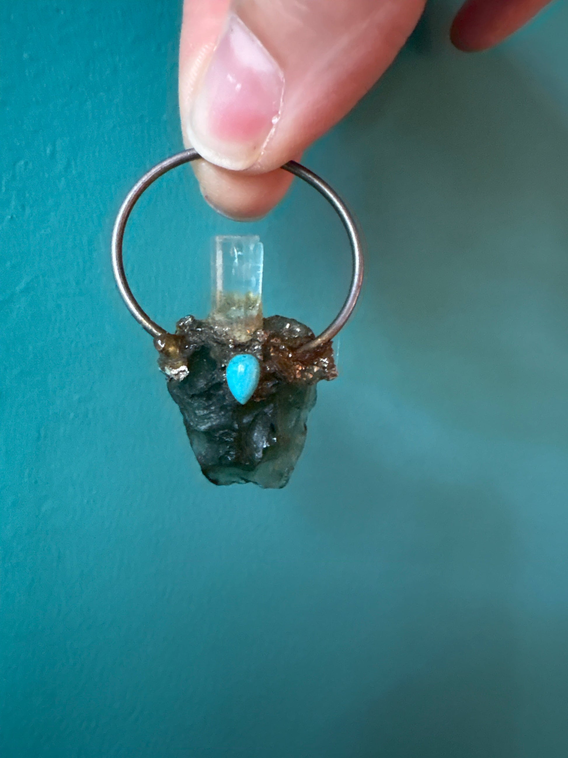 Custom made by Syd pendant featuring aquamarine, turquoise, and moldavite gemstones on a metal hoop.