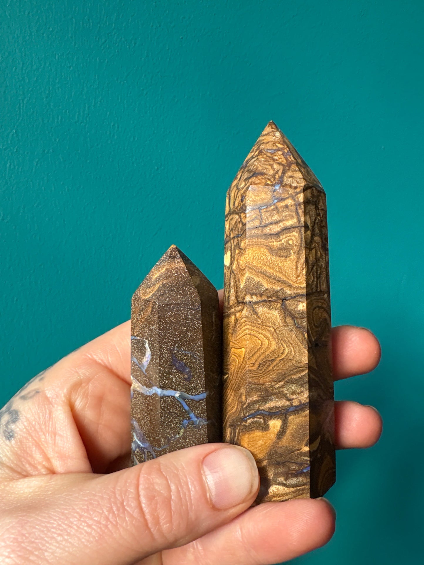 Hand holding two polished River Veined Opal Towers with unique swirling patterns against a teal background