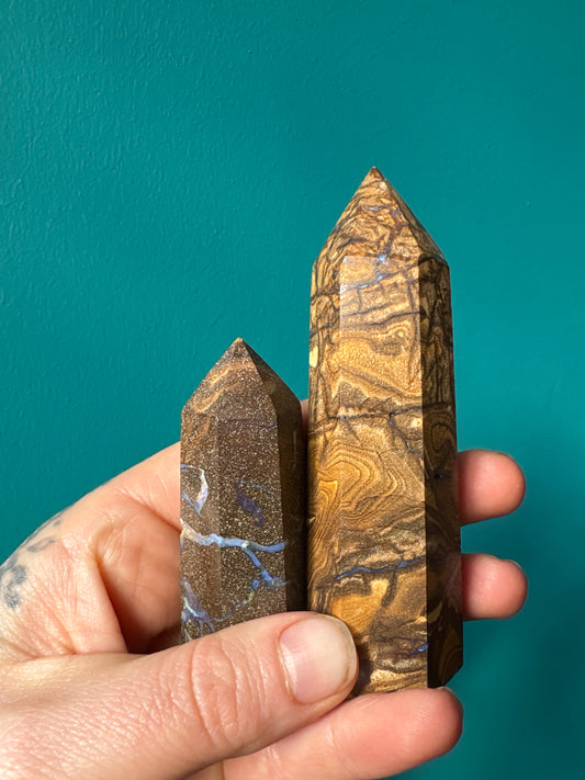 Hand holding two polished River Veined Opal Towers with unique swirling patterns against a teal background
