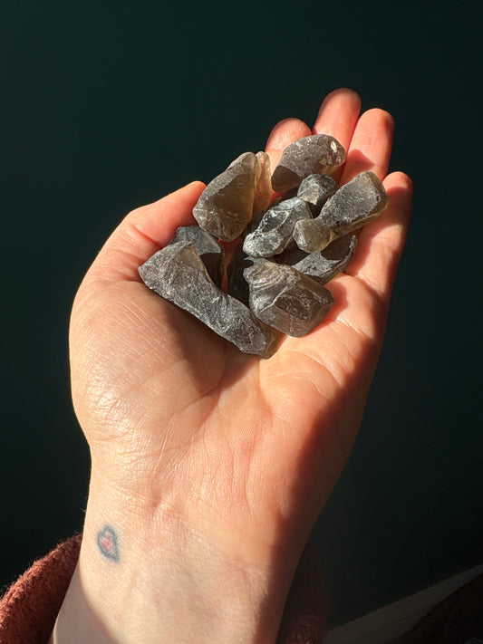 Hand holding tumble semi polished rough raw smokey quartz stones against dark background