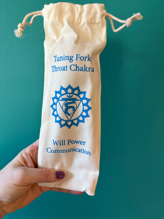 Hand holding a beige drawstring pouch with blue text and throat chakra symbol labeled "Tuning Fork Throat Chakra Will Power Communication"