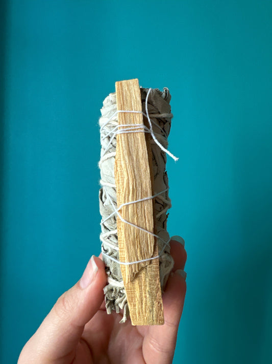White Sage and Palo Santo Smudge Stick held against blue background for cleansing and purification
