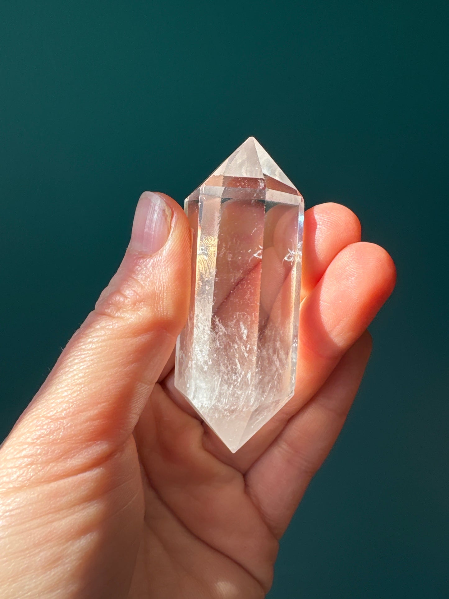 Hand holding a clear double terminated clear quartz crystal against a dark green background