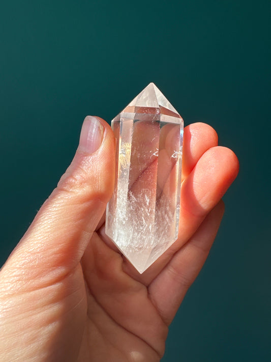 Hand holding a clear double terminated clear quartz crystal against a dark green background