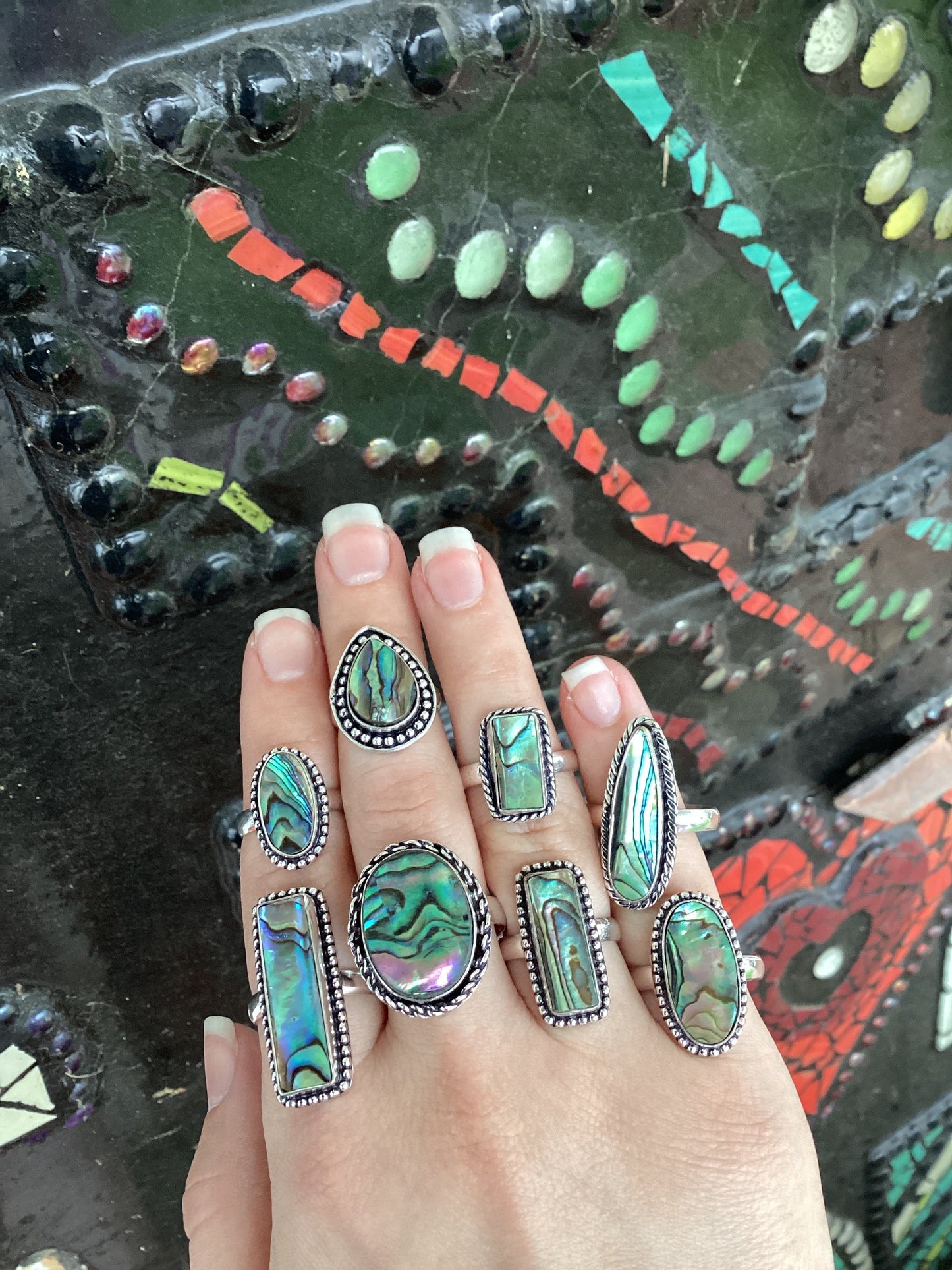 Close-up of a hand wearing multiple silver-plated abalone rings with colorful iridescent patterns.