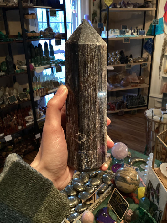 Hand holding a polished tower-shaped blue sapphire crystal in a store with various crystals and stones in the background