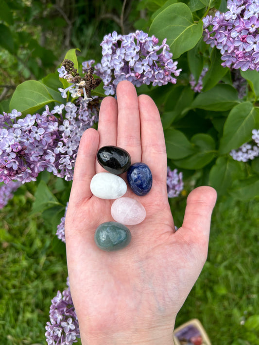 Hand holding assorted mini crystal eggs with lilac flowers in the background